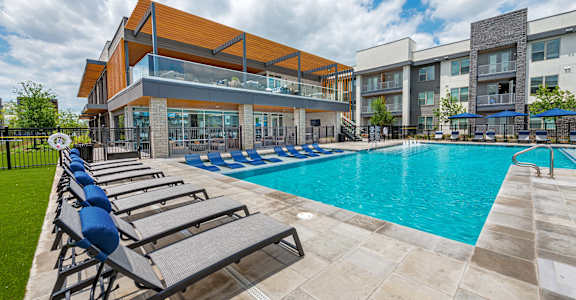 A large swimming pool with sun loungers in front of a modern building.
