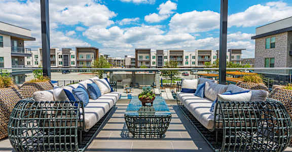 A patio with two black wicker sofas and a table with a vase of flowers on it.
