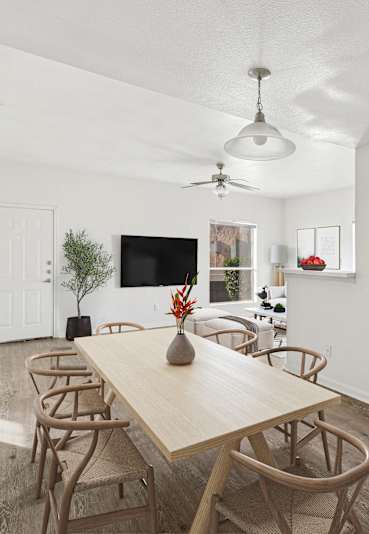 Modern dining area with a light wood table, woven chairs, and minimalist décor in an open-concept space.