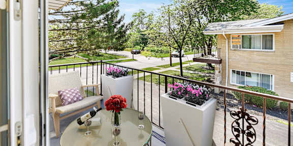A balcony with a glass table and chairs overlooking a garden.