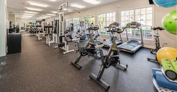 a spacious fitness center with cardio equipment and windows