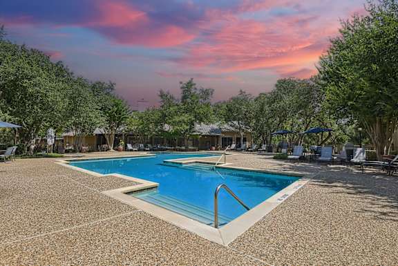A large swimming pool surrounded by trees and chairs.
