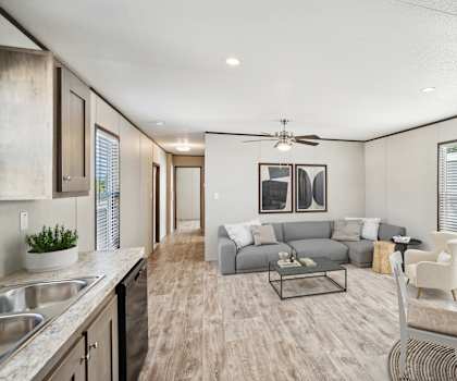 A modern kitchen and living room with a grey sofa and a dining table at Converse Meadows MHC in Converse, TX