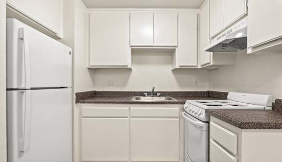 A white kitchen with a refrigerator, sink, and stove.