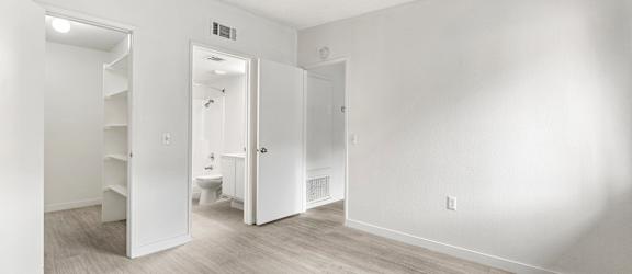 A white room with a wooden floor and a toilet in the background.