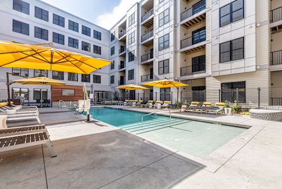 a swimming pool with yellow umbrellas in front of an apartment building