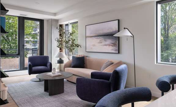 A living room with a grey rug and a large painting on the wall.