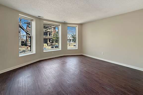 A spacious room with wooden flooring and large windows.