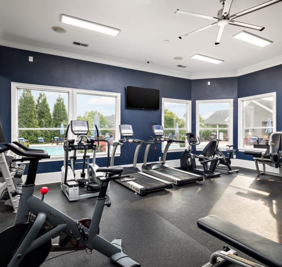a gym with cardio equipment and windows with a view of a pool
