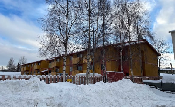 Apartment building with snow on the ground and trees in the background. at Nicole Apartments, Anchorage, AK