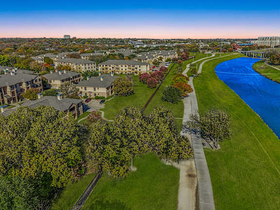 A river flows through a green park with apartment buildings in the background  at The Canyons Apartments, Texas, 76116