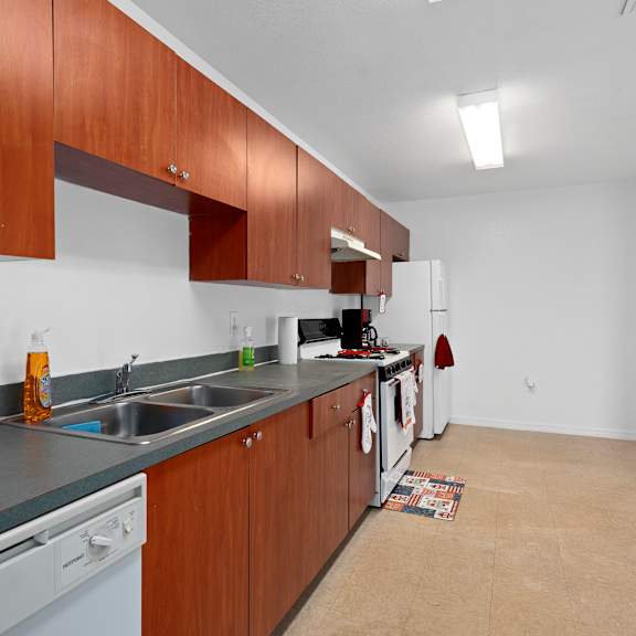 A kitchen with wooden cabinets and a white dishwasher at The Groves at Wimauma Apartments , Wimauma, Florida