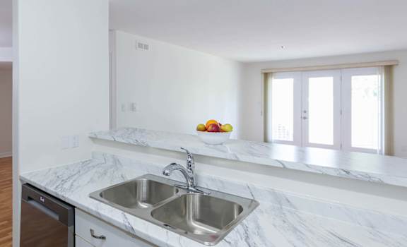 A kitchen with a marble countertop and a stainless steel sink.