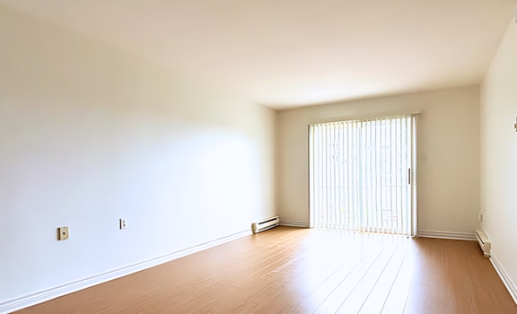 A room with wooden flooring and a window with blinds.