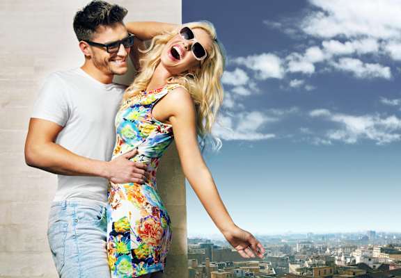 a young couple standing on top of a building with a view of the city behind them