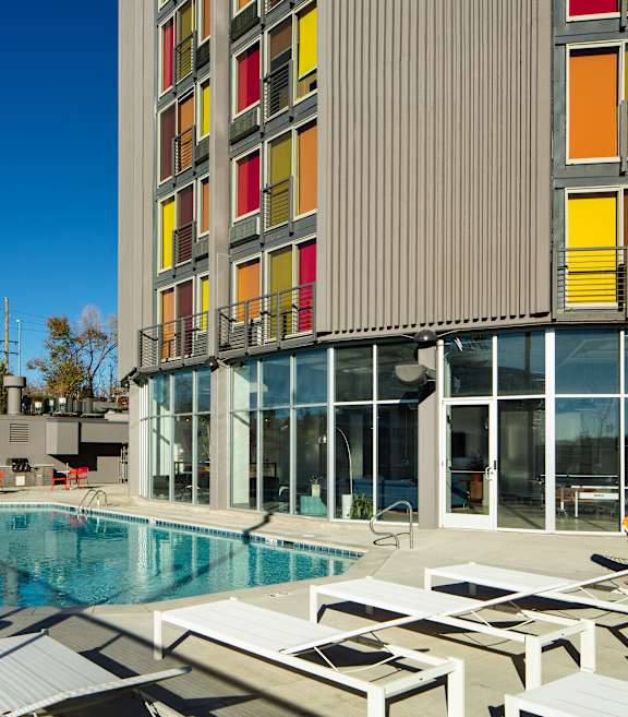 A swimming pool with sun loungers and a building with red, yellow and orange windows.