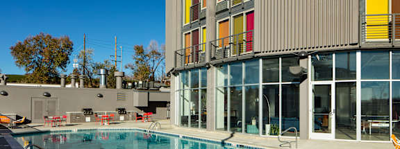 A swimming pool with sun loungers and a building with red, yellow and orange windows.