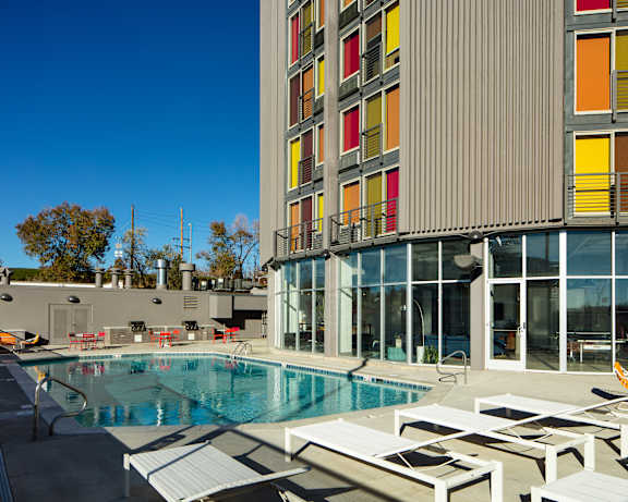 A swimming pool with sun loungers and a building with red, yellow and orange windows.