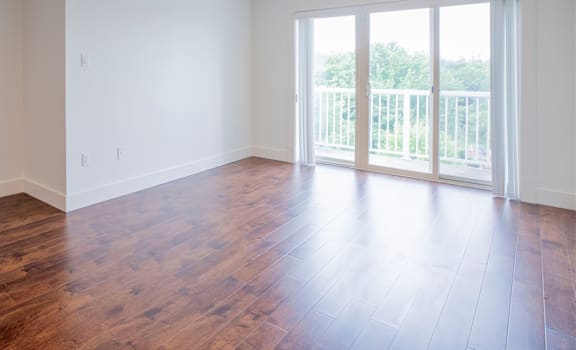 A room with wooden floors and a sliding glass door leading to a balcony.