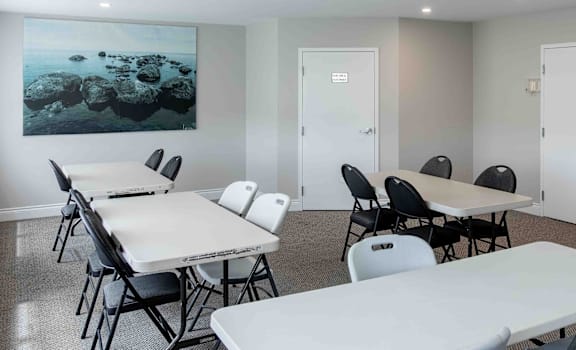 A room with white tables and chairs and a painting on the wall.