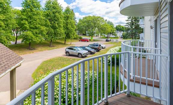 A view from a balcony overlooking a parking lot and trees.