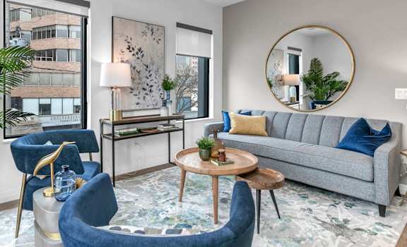 A living room with a grey couch, blue armchair, and a round mirror.