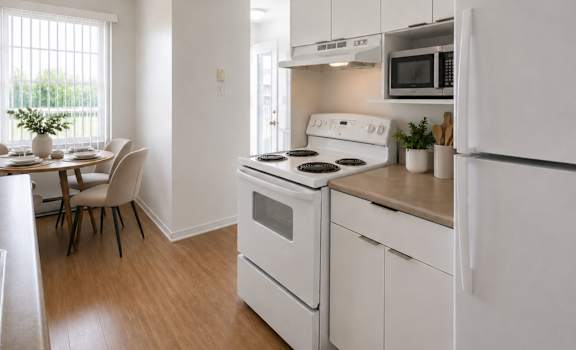 A white kitchen with a stove, refrigerator, and dining table.