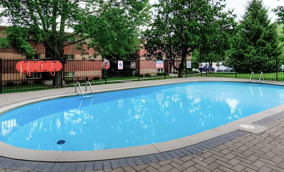 A small pool surrounded by trees and a black fence.