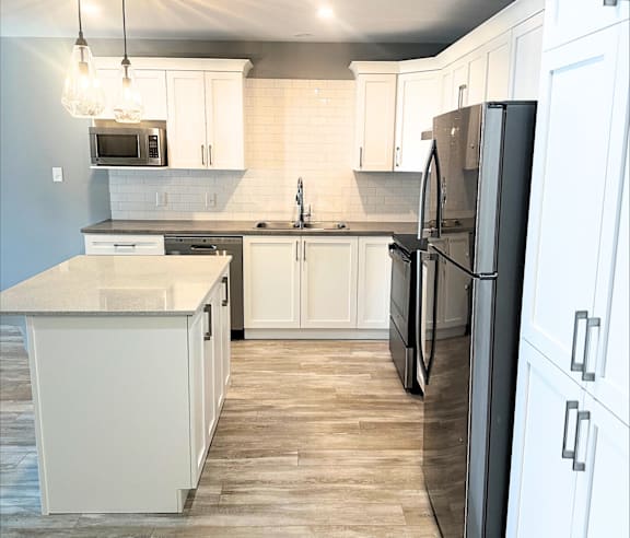 A modern kitchen with a stainless steel refrigerator and wooden flooring.