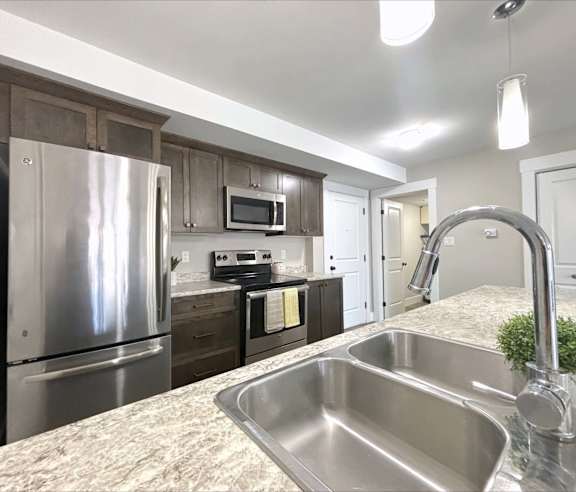 A modern kitchen with a stainless steel refrigerator and wooden flooring.