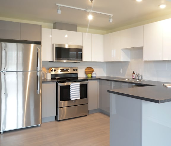 A modern kitchen with a stainless steel refrigerator and wooden flooring.