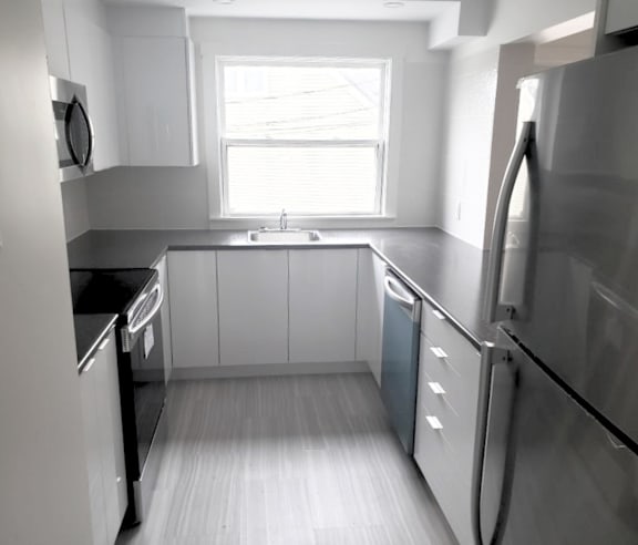A modern kitchen with a stainless steel refrigerator and wooden flooring.