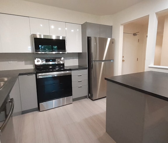 A modern kitchen with a stainless steel refrigerator and wooden flooring.
