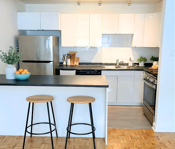A modern kitchen with a stainless steel refrigerator and wooden flooring.