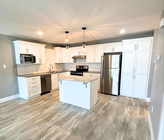 A modern kitchen with a stainless steel refrigerator and wooden flooring.