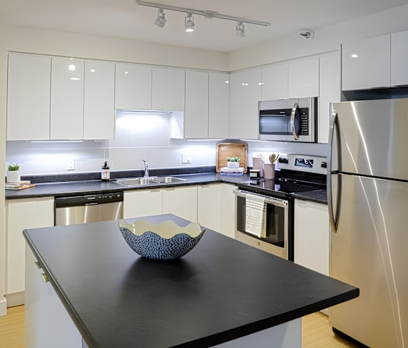 A modern kitchen with a stainless steel refrigerator and wooden flooring.