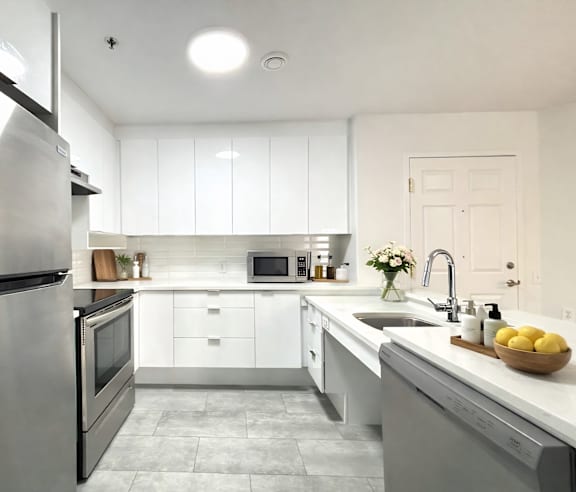 A modern kitchen with a stainless steel refrigerator and wooden flooring.