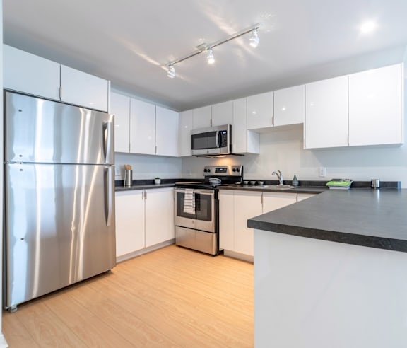 A modern kitchen with a stainless steel refrigerator and wooden flooring.
