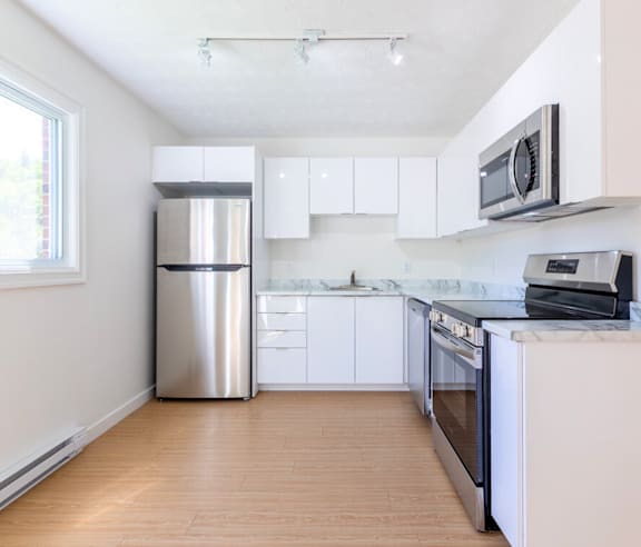 A modern kitchen with a stainless steel refrigerator and wooden flooring.
