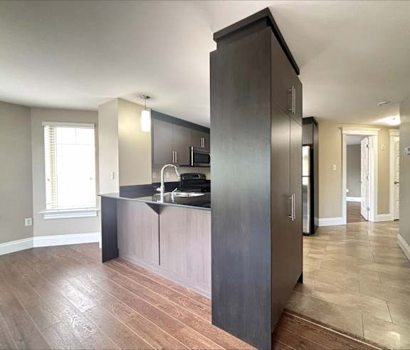 A modern kitchen with a stainless steel refrigerator and wooden flooring.
