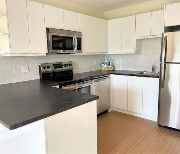 A modern kitchen with a stainless steel refrigerator and wooden flooring.