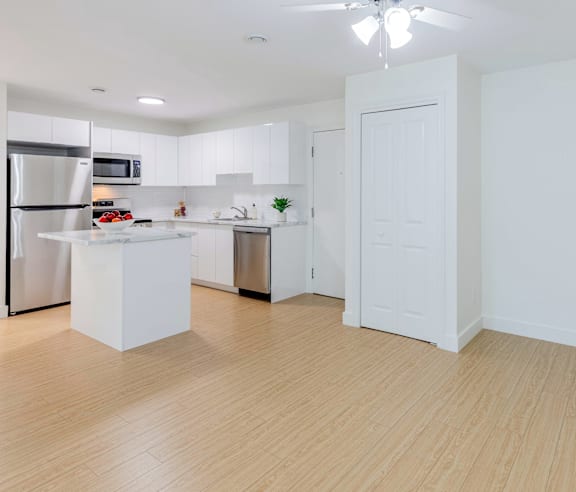 A modern kitchen with a stainless steel refrigerator and wooden flooring.