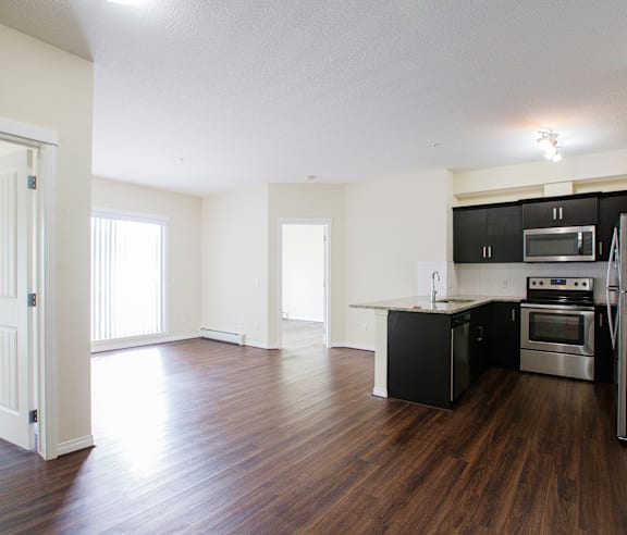 A modern kitchen with a stainless steel refrigerator and wooden flooring.