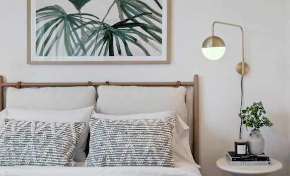 a bedroom with a bed with white sheets and pillows and a picture of plants
