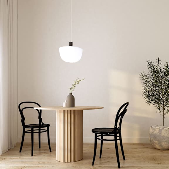 A dining room table with two black chairs, a hanging light, and a potted plant.