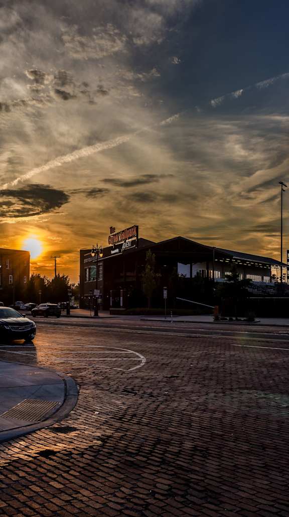A sunset view of a street with cars parked on the side.