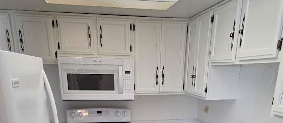 A kitchen with white appliances and a stone wall.