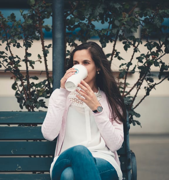 a woman sitting on a bench drinking a cup of coffee