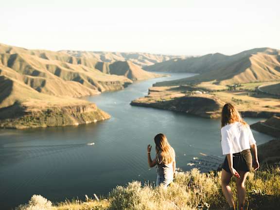 Two people are standing on a hill overlooking a river.
