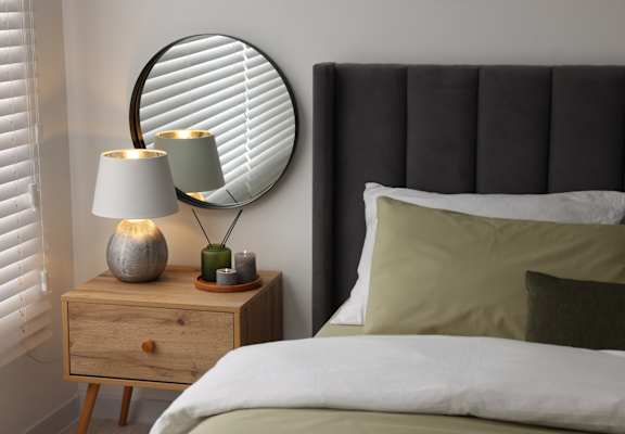 A bedroom with a bed, a nightstand with a lamp and a round mirror on the wall.